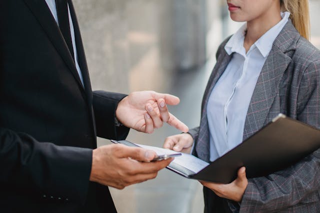 A man and woman in suits discuss terms of a contract that she is holding. Image at PrimeOfficeSpace.co.uk.