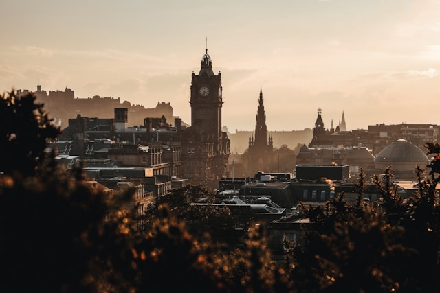 A view across Edinburgh at dusk from on top of Calton Hill. Some Gothic church spires rise up above the historic cityscape, and the buildings are cast in a dramatic contrast of light and dark from the pale light of the setting sun. Image at LondonOfficeSpace.com.