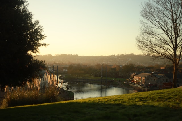 Looking down from atop a grassy bankside hill to the Quay in Exeter. The sun is setting over the river Exe, with a view of the hills and countryside in the distance. Image at LondonOfficeSpace.com.